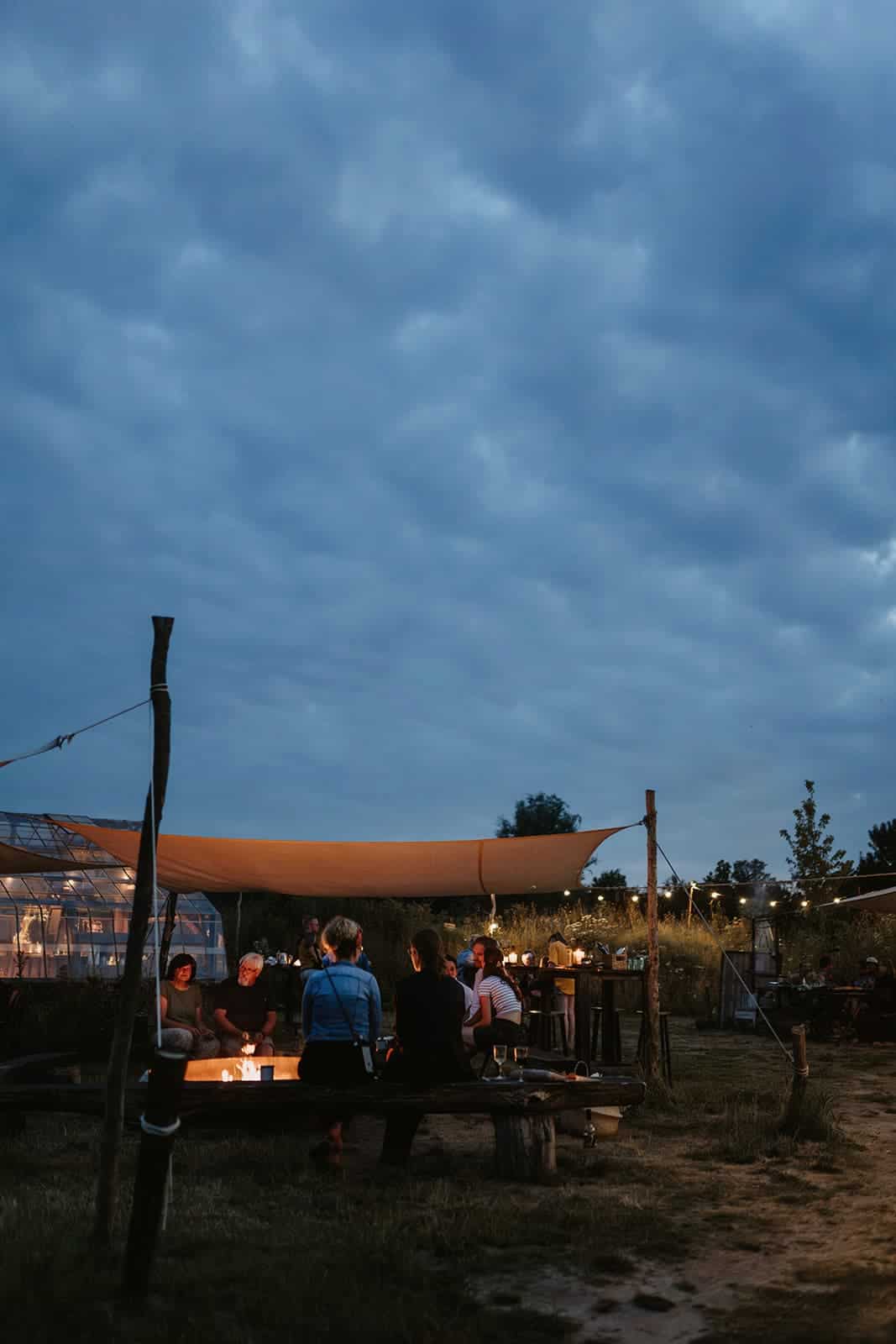 Gäste sitzen am Abend gemeinsam am Feuer unter freiem Himmel
