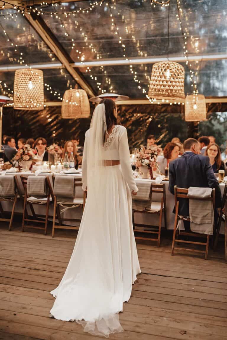 Braut steht am Kopf einer langen Tafel unter dem Zelt bei einer Outdoor Hochzeit im Rahmen eines Wedding Weekends