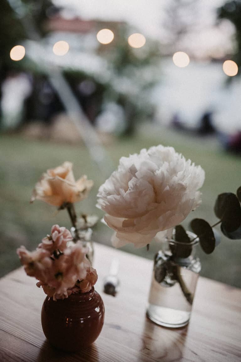 Florales Tischdetail mit Kerzen und Pfingstrosen bei einer Outdoor-Hochzeit an einem stilvollen Ferienhaus.