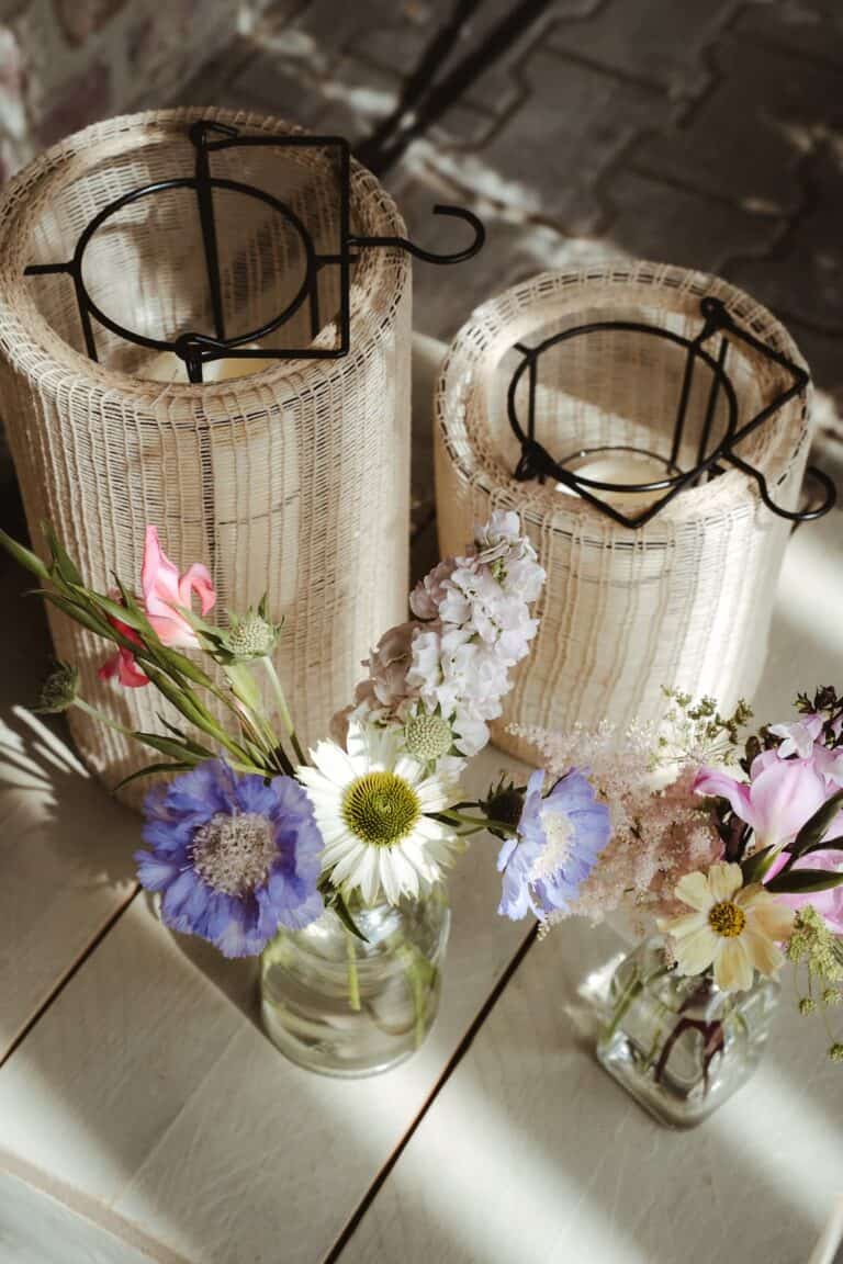 Florale Detailaufnahme mit Windlichtern und Sommerblumen auf Holztisch – natürliche Dekoration im Rahmen einer hochwertig geplanten Zelthochzeit.