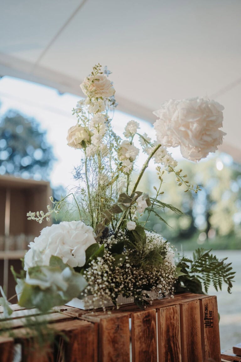 Bar-Setup in Holzoptik mit floralen Details bei einer Outdoor-Hochzeit, organisiert durch professionelle Hochzeits- und Eventplanung.