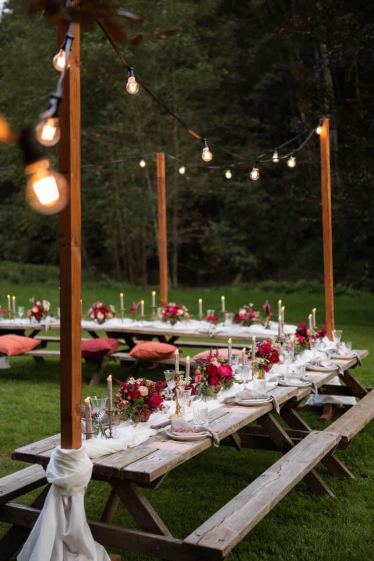 Lange Holztafeln im Picknick Style unter Lichterketten als gemeinsames Dinner bei einem entspannten Outdoor Wedding-Weekend.