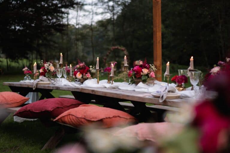Lange Tafel unter freiem Himmel mit Kerzen, floraler Tischdekoration und Sitzkissen – stimmungsvolles Dinner bei einer Outdoor Hochzeit in einem AirBnB in Belgien.