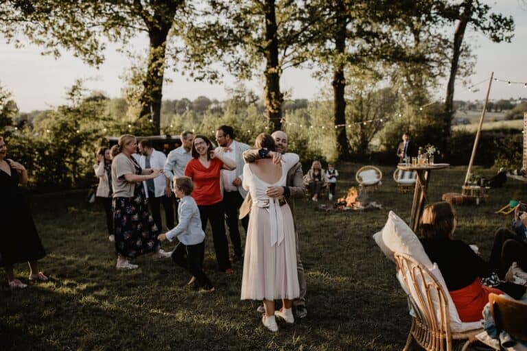 Gäste tanzen und umarmen sich bei einer Outdoor-Hochzeit in stimmungsvoller Dämmerung am Lagerfeuer.