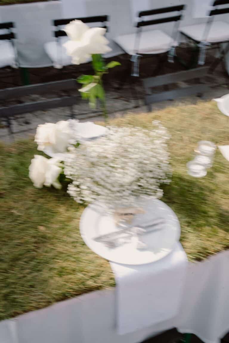 Bewegtes Tischdetail mit floralen Elementen bei einer Outdoor-Hochzeit, eingefangen zwischen Struktur und Lebendigkeit.