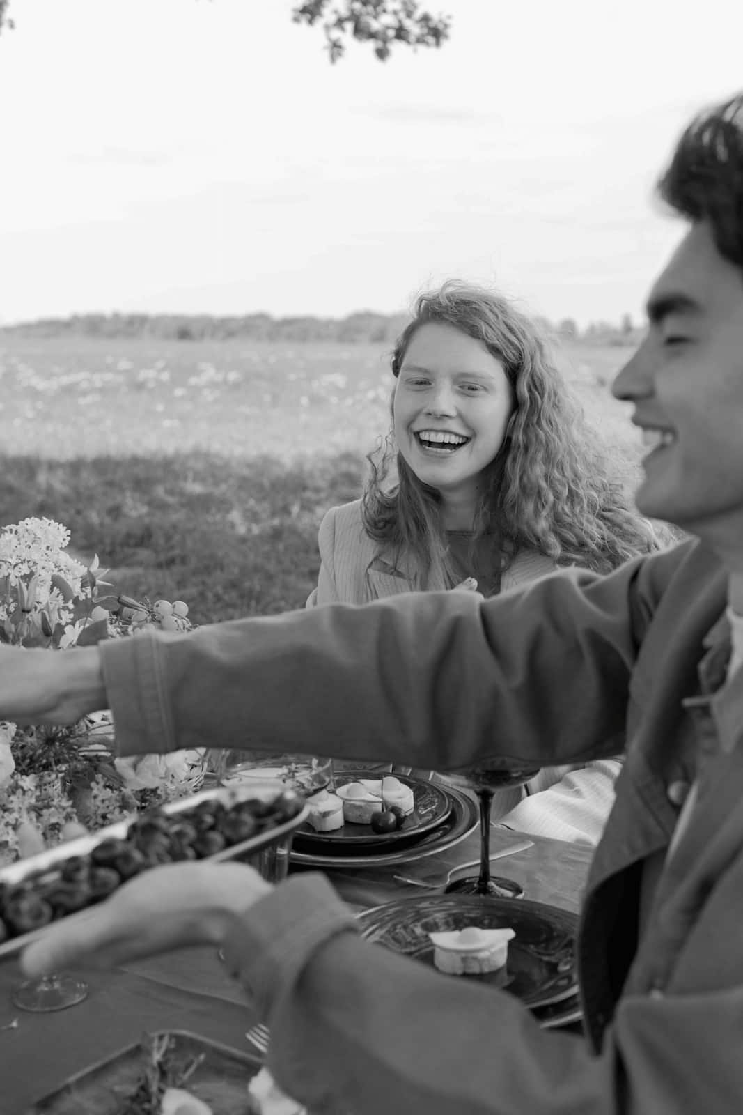 Fröhliche Gäste genießen gemeinsam ein entspanntes Dinner an einer gedeckten Tafel im Grünen – Zeit für echte Begegnungen bei einem mehrtägigen Wedding Weekend.