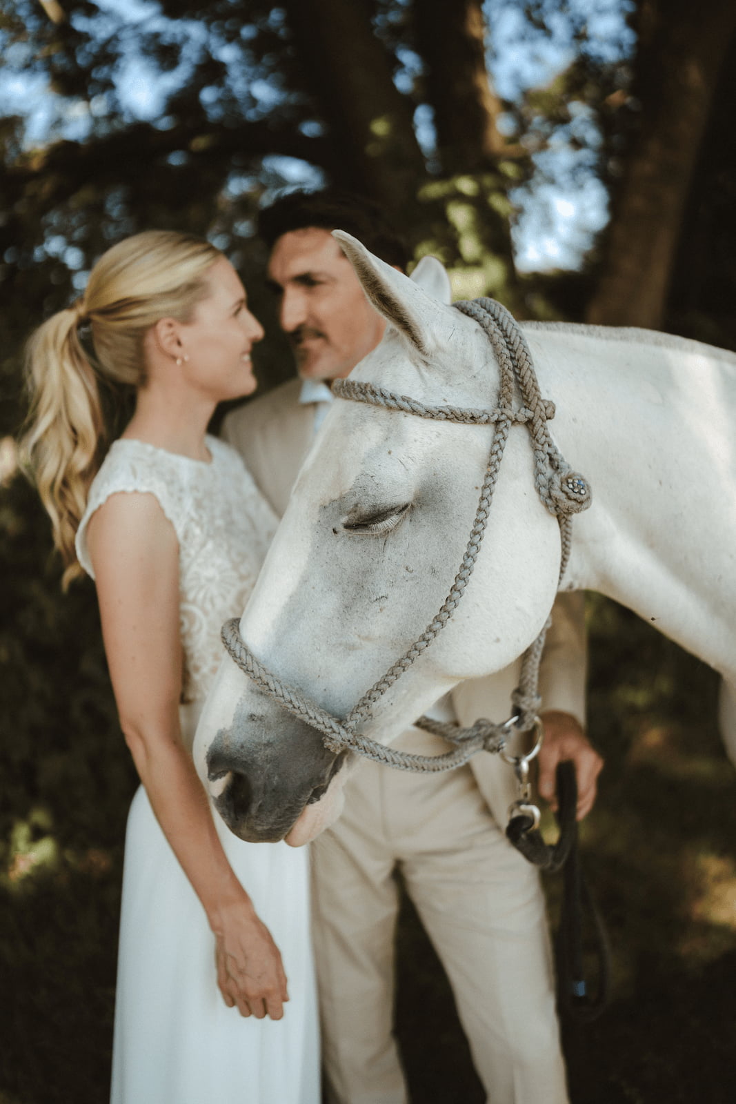 Lucia und Philipp mit ihrem weißen Pferd bei ihrer Gartenhochzeit auf dem eigenen Familien-Pferdehof – eine persönliche Hochzeit zu Hause, geplant vom Hochzeitsplaner Team von Hey Happy Day Hochzeitsplanung und Events.