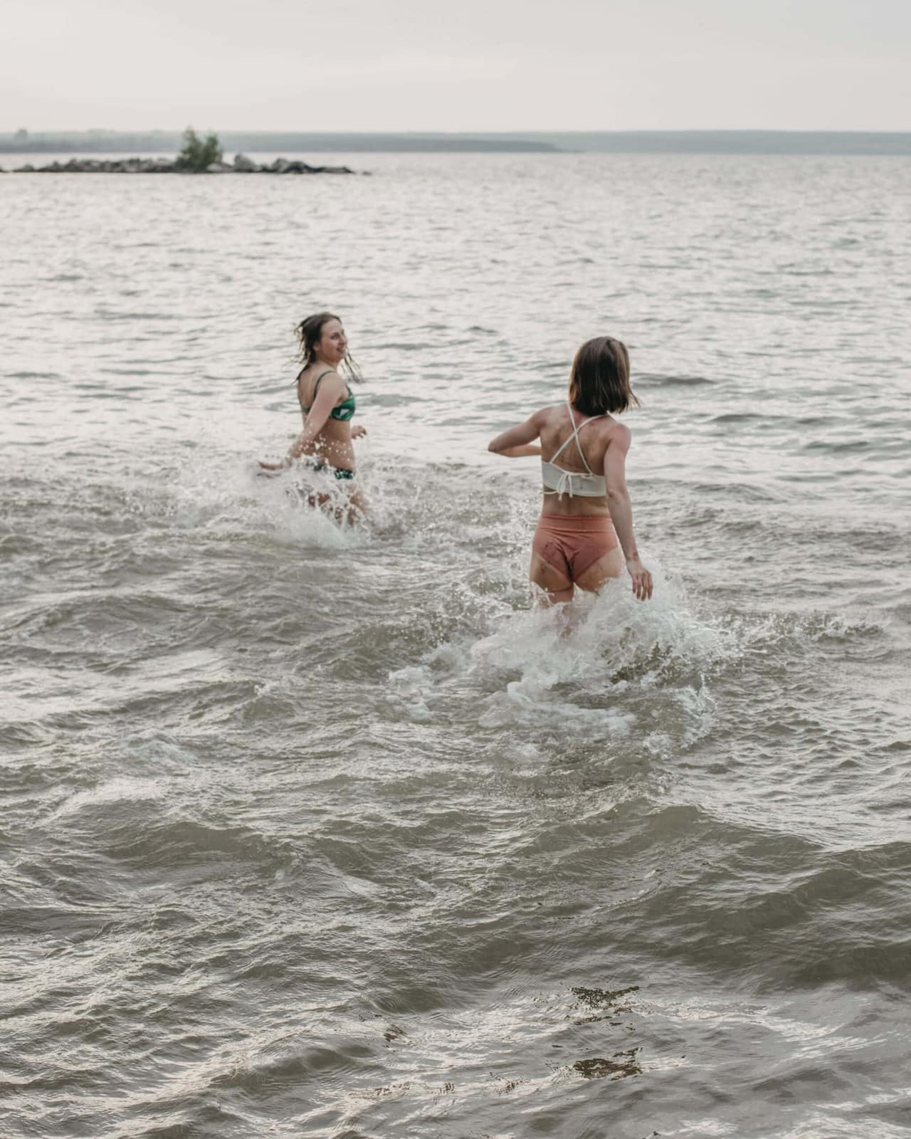 Zwei Gäste laufen lachend in einen See und genießen ihre gemeinsame Zeit am Wasser – ungezwungene Erlebnisse abseits des Hochzeitstags bei einem Wedding Weekend.