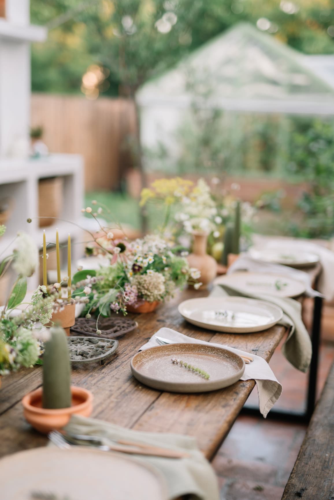 Liebevoll gedeckte Holztafel mit natürlicher Wiesenfloristik, Kerzen und handgefertigtem Geschirr im Grünen – entspanntes Dinner bei einem Wedding Weekend geplant vom Hey Happy Day Weddingplanner Team anlässlich einer Hochzeit in der Toskana.