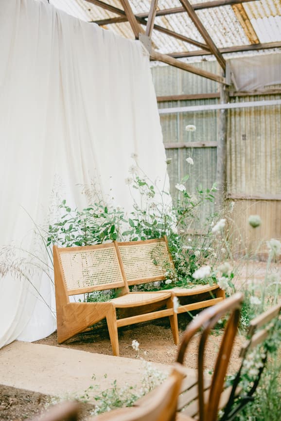 Kleine Holzbank mit Wiener Geflecht, umgeben von zarten Wiesenblumen und Gräsern – liebevoll gestalteter Trauungsplatz von Hey Happy Day Hochzeitsplanung für ein persönliches Wedding Weekend.